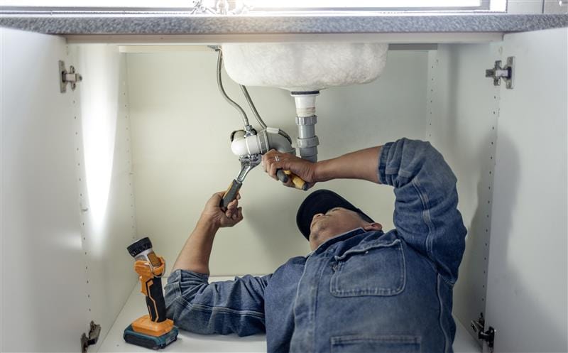 Plumber repairing pipes beneath a bathroom sink in Largo