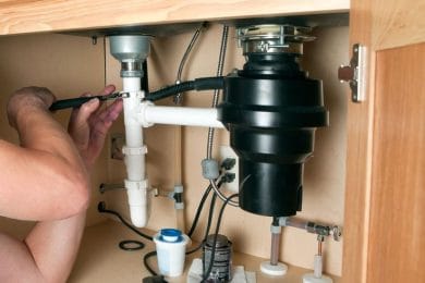 Plumber repairing a garbage disposal beneath a kitchen sink in Largo