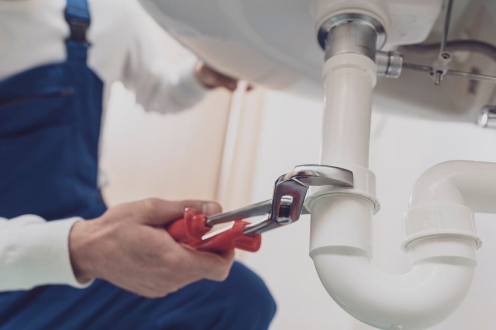 Plumber repairing a white drain pipe beneath a sink in Largo