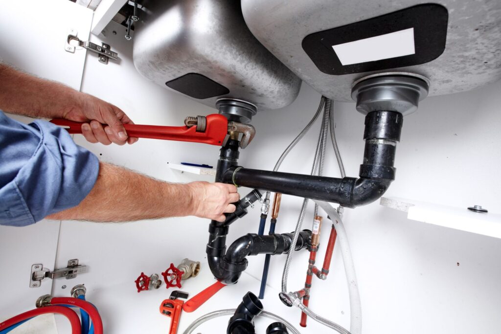 Plumber repairing drain pipes beneath a kitchen sink in Largo